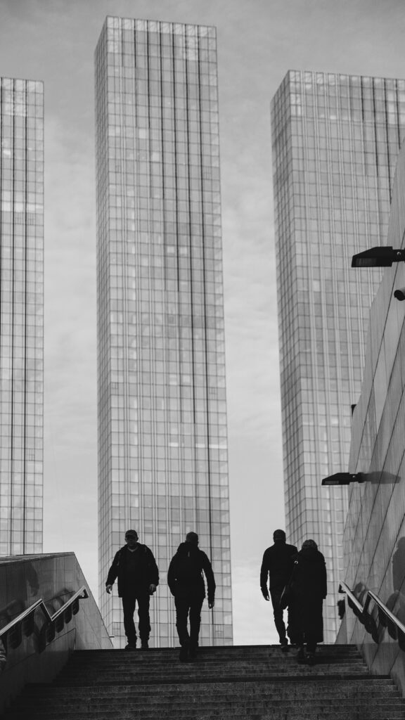 Silhouetted pedestrians in an urban landscape by skyscrapers in black and white.