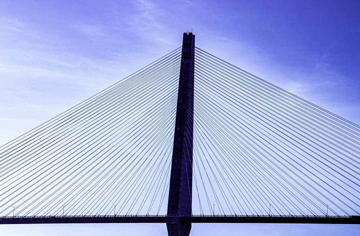 A modern cable-stayed bridge viewed from below with a clear blue sky backdrop.