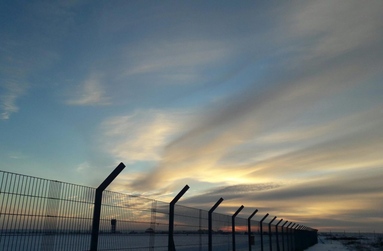 A striking sunset with dramatic clouds over a silhouetted industrial fence.