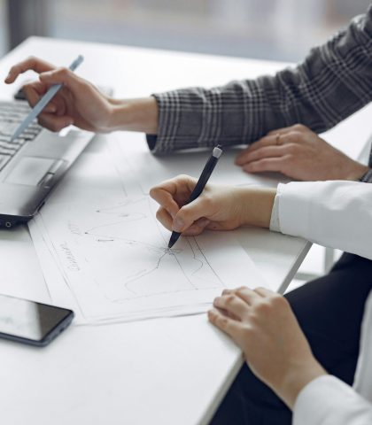 Two professionals collaborating on business plans using a laptop and paper documents.