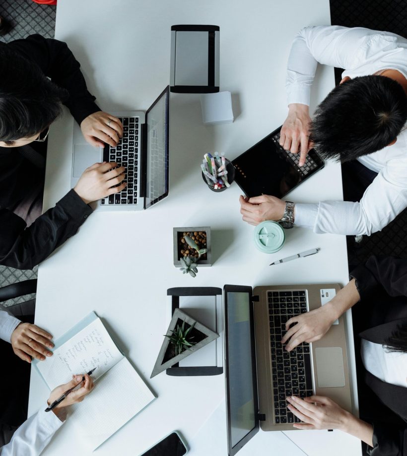 A diverse team working together in a modern office setting, focusing on laptops and collaboration.