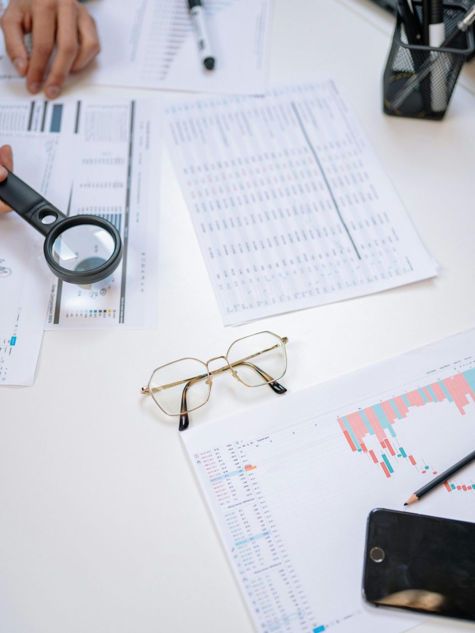 Flat lay of business documents with magnifying glass, glasses, and smartphone on a desk.