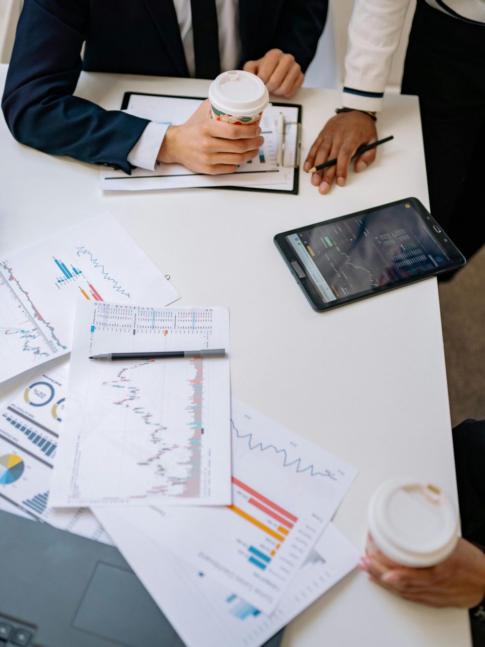 High-angle view of office meeting with charts, coffee, and tablet device.