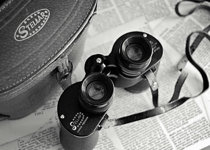 Classic vintage binoculars with a leather case laid on open newspapers, evoking nostalgia.