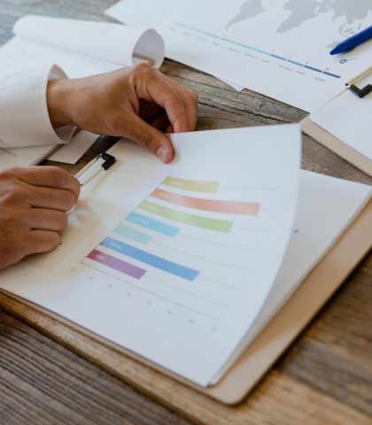Close-up of hands reviewing business report with colorful charts and graphs on a wooden desk.